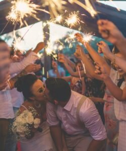 Bride and Groom seal a kiss while exiting Ceremony with crowd holding sparklers.